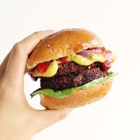 Holding a Quinoa Black Bean Beet Burger held between two halves of a bun