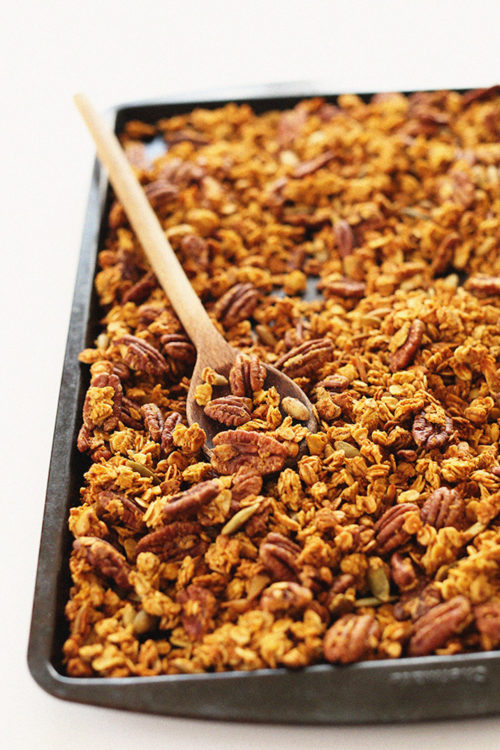 Using a wooden spoon to stir a tray of Pumpkin Pecan Granola