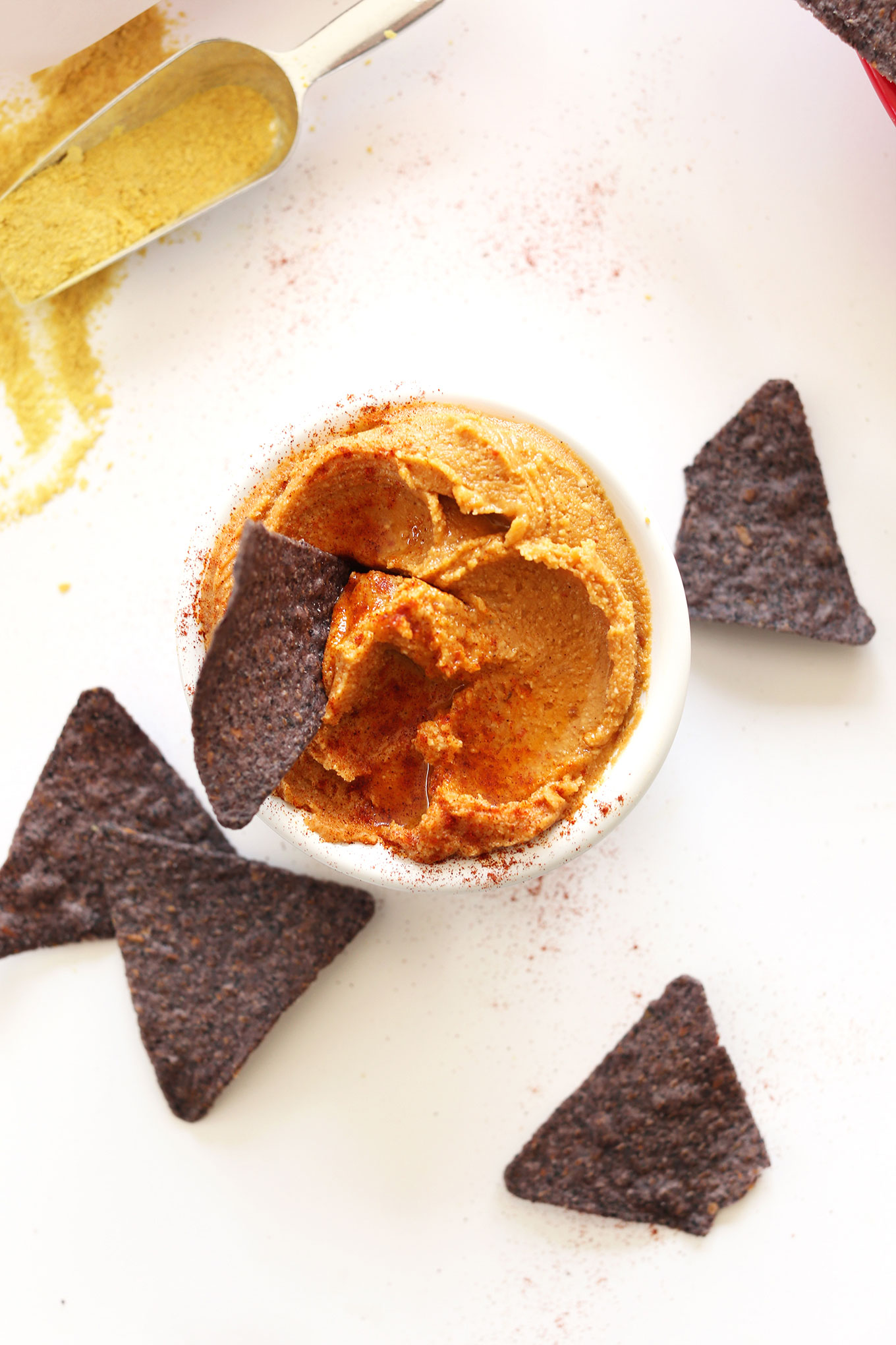 Dipping a blue corn tortilla chip into a bowl of Spreadable Vegan Cheese