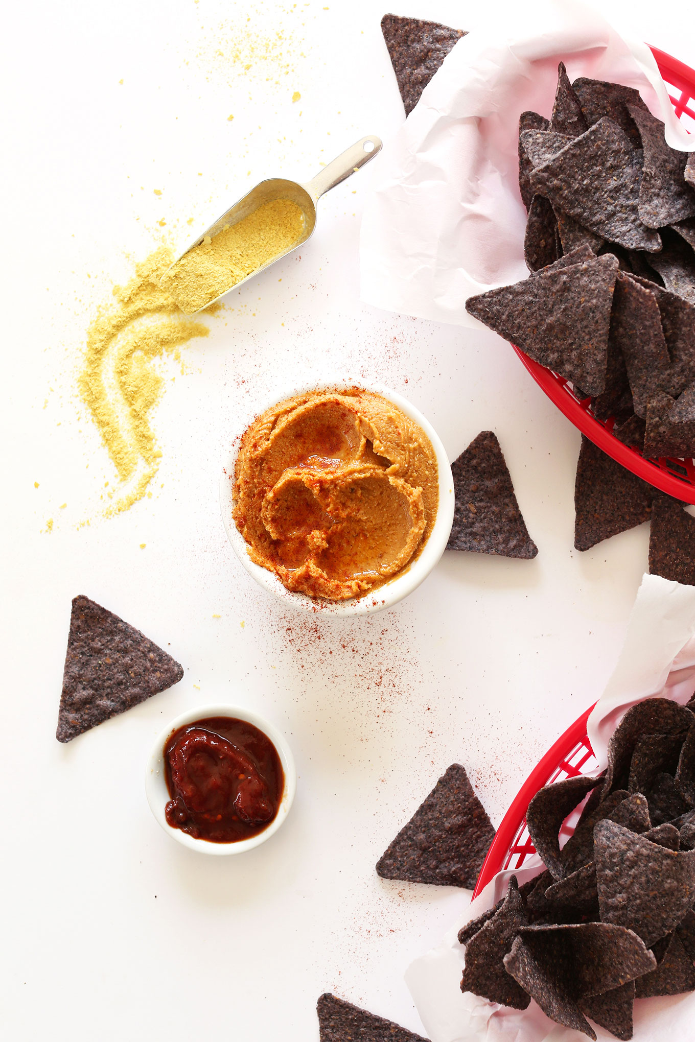 Bowl of Vegan Mexican Cheese with a basket of blue corn tortilla chips and other ingredients used to make it