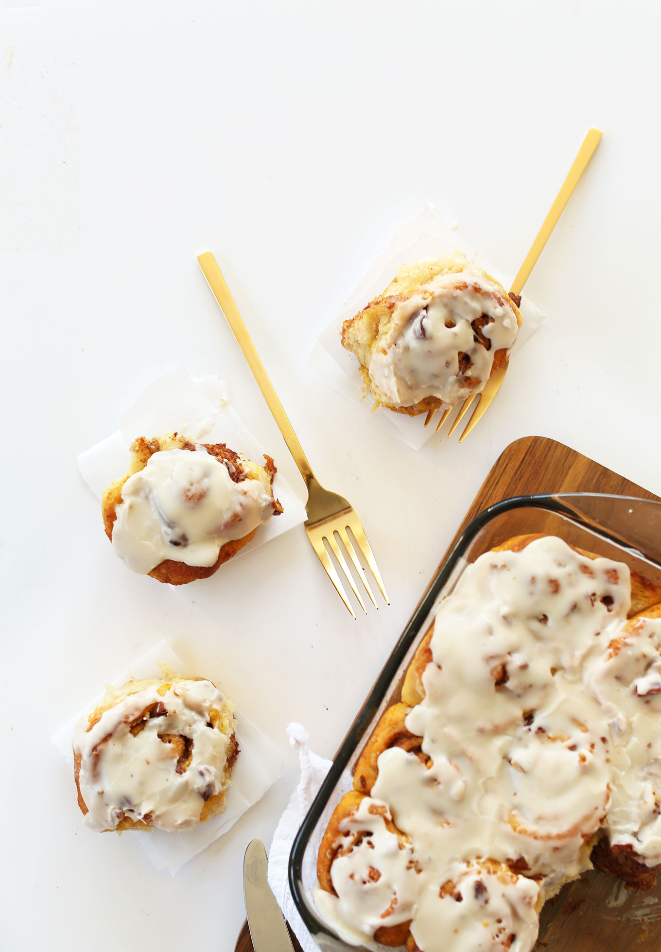 Three of our Vegan Pumpkin Cinnamon Rolls on parchment paper alongside a pan of more