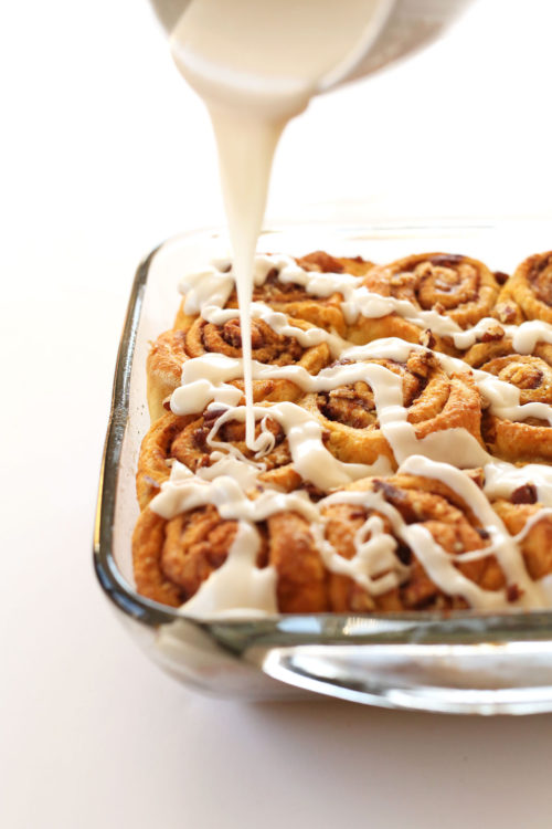 Drizzling glaze over a batch of Vegan Pumpkin Cinnamon Rolls