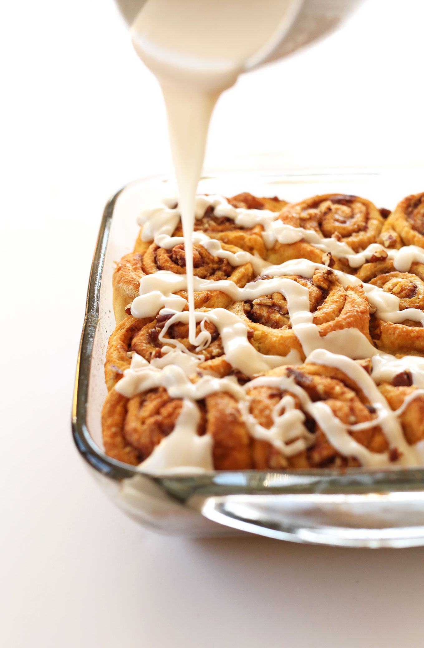 Pouring glaze onto a pan of Vegan Pumpkin Cinnamon Rolls