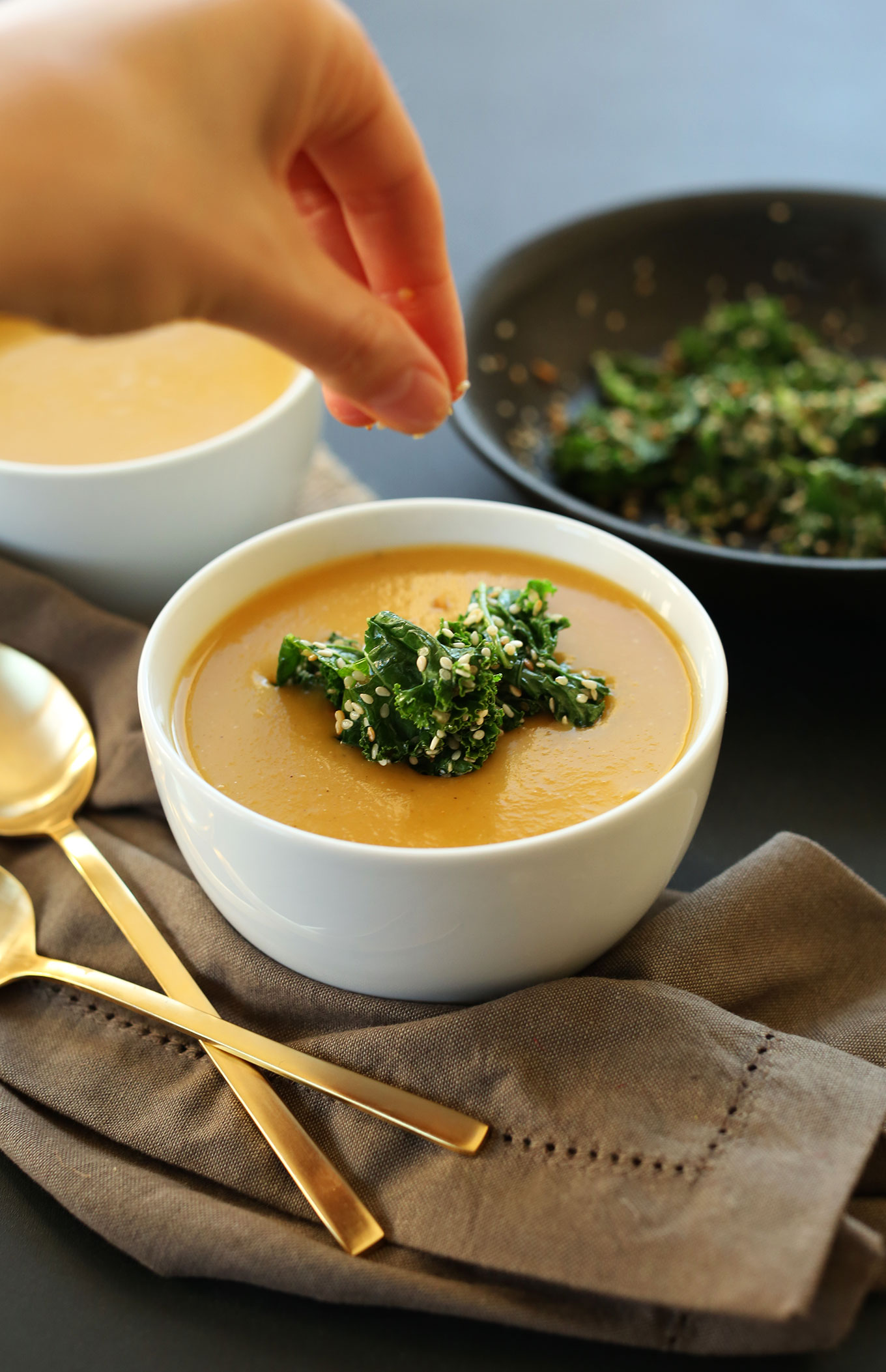 Sprinkling sesame seeds onto a bowl of pumpkin soup topped with kale
