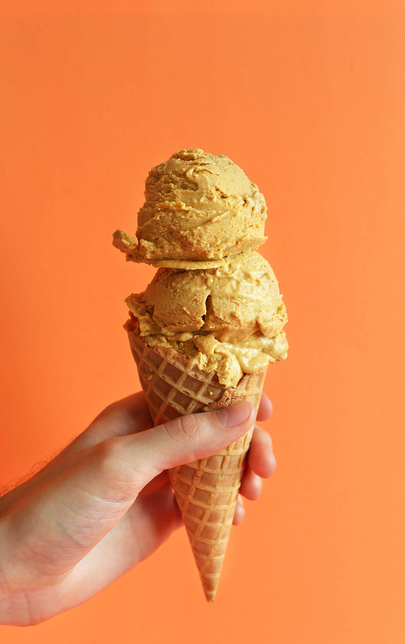 Holding a waffle cone topped with double-scooped homemade Pumpkin Ice Cream