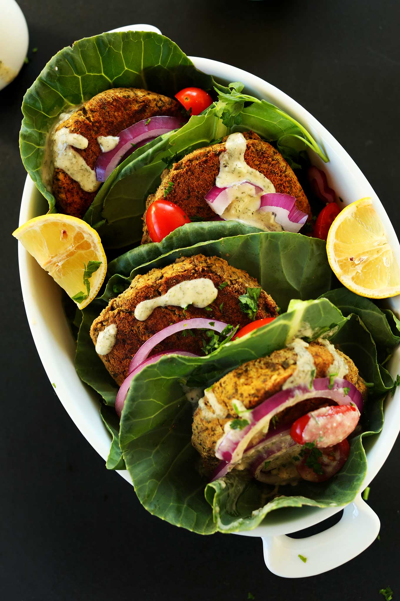 Large dish of falafel burgers wrapped in collard greens with onions, sauce, and other toppings
