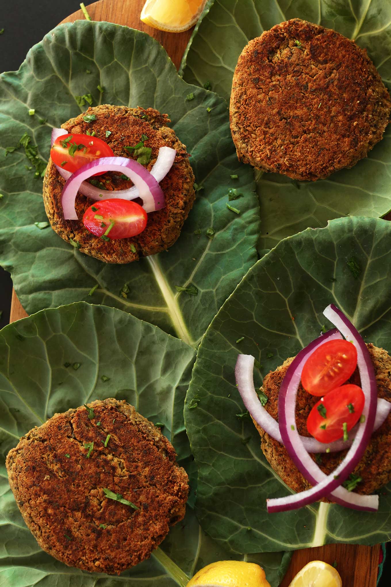 Cutting board with collard green leaves topped with falafel burgers and other toppings