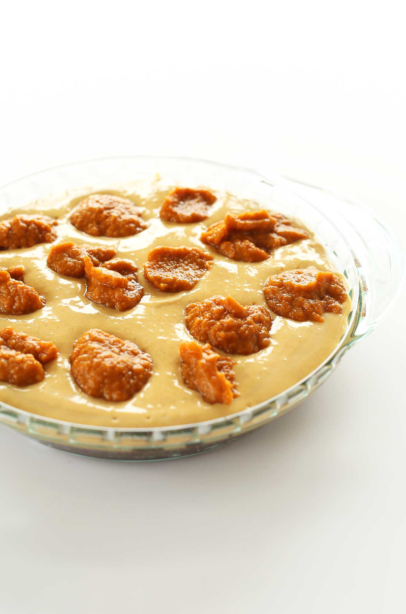 Pie pan with vegan cheescake batter and dollops of pumpkin for swirling