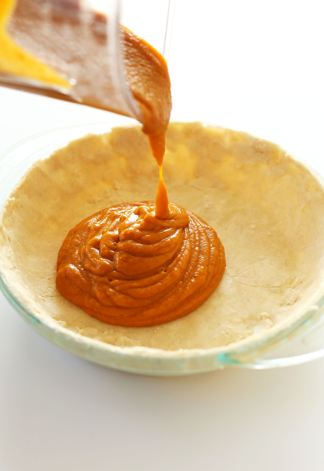 Pouring vegan pumpkin pie filling into a gluten-free pie crust