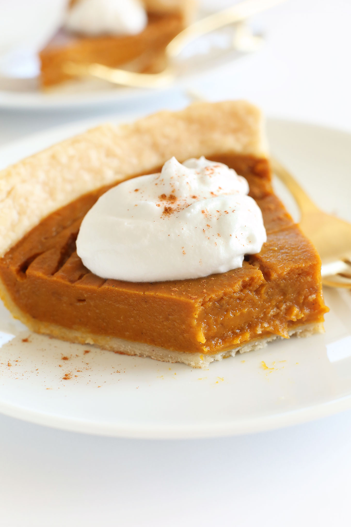 Partially eaten slice of pumpkin pie topped with coconut whipped cream