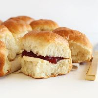Batch of homemade Dinner Rolls with one having vegan butter and jam in the middle