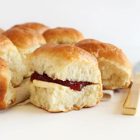 Batch of homemade Dinner Rolls with one having vegan butter and jam in the middle
