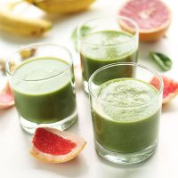 Three glasses of our Grapefruit Green Smoothie surrounded by ingredients used to make it