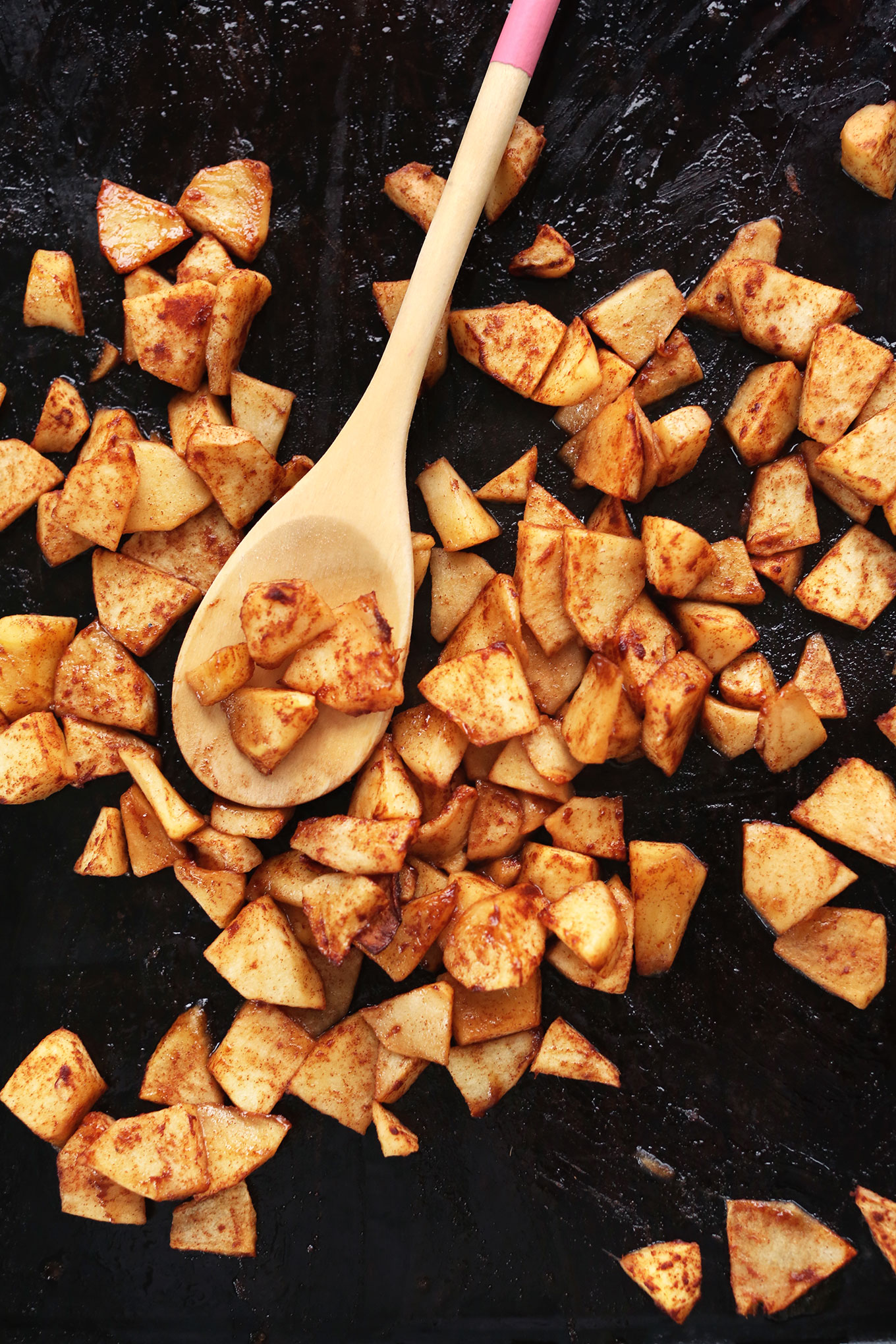 Stirring apples on a baking sheet for a homemade vegan snack