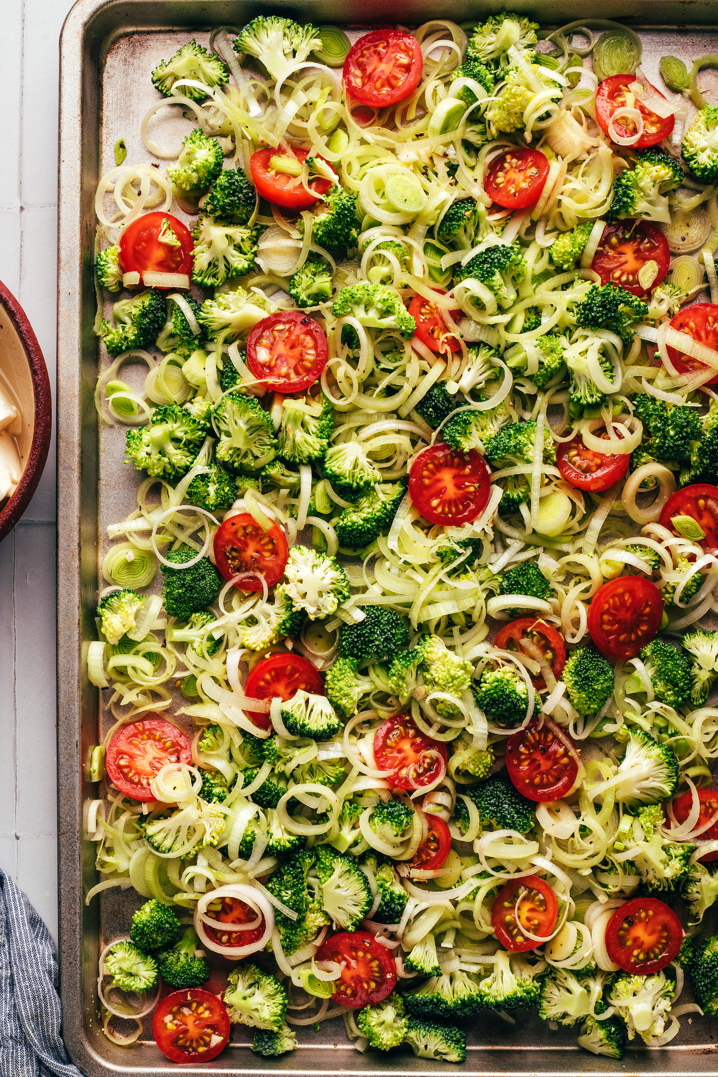 Broccoli, leeks, and cherry tomatoes on a baking sheet