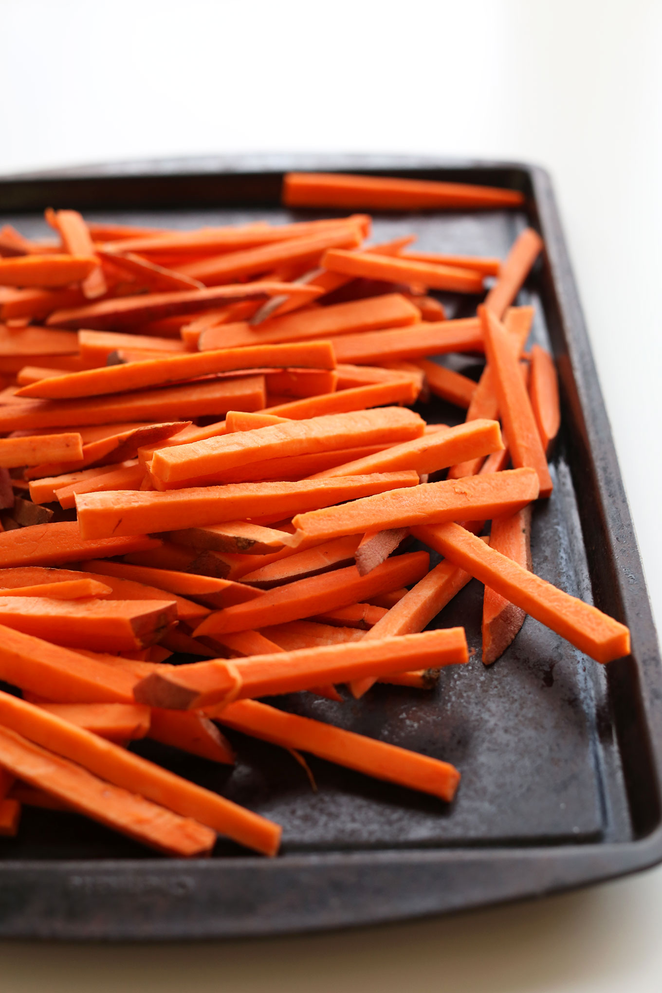 Baking sheet filled with sliced sweet potatoes for homemade fries