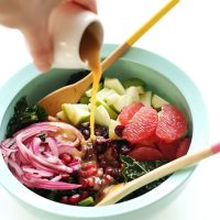 Pouring Red Wine Vinaigrette onto a big bowl of Kale Citrus Salad