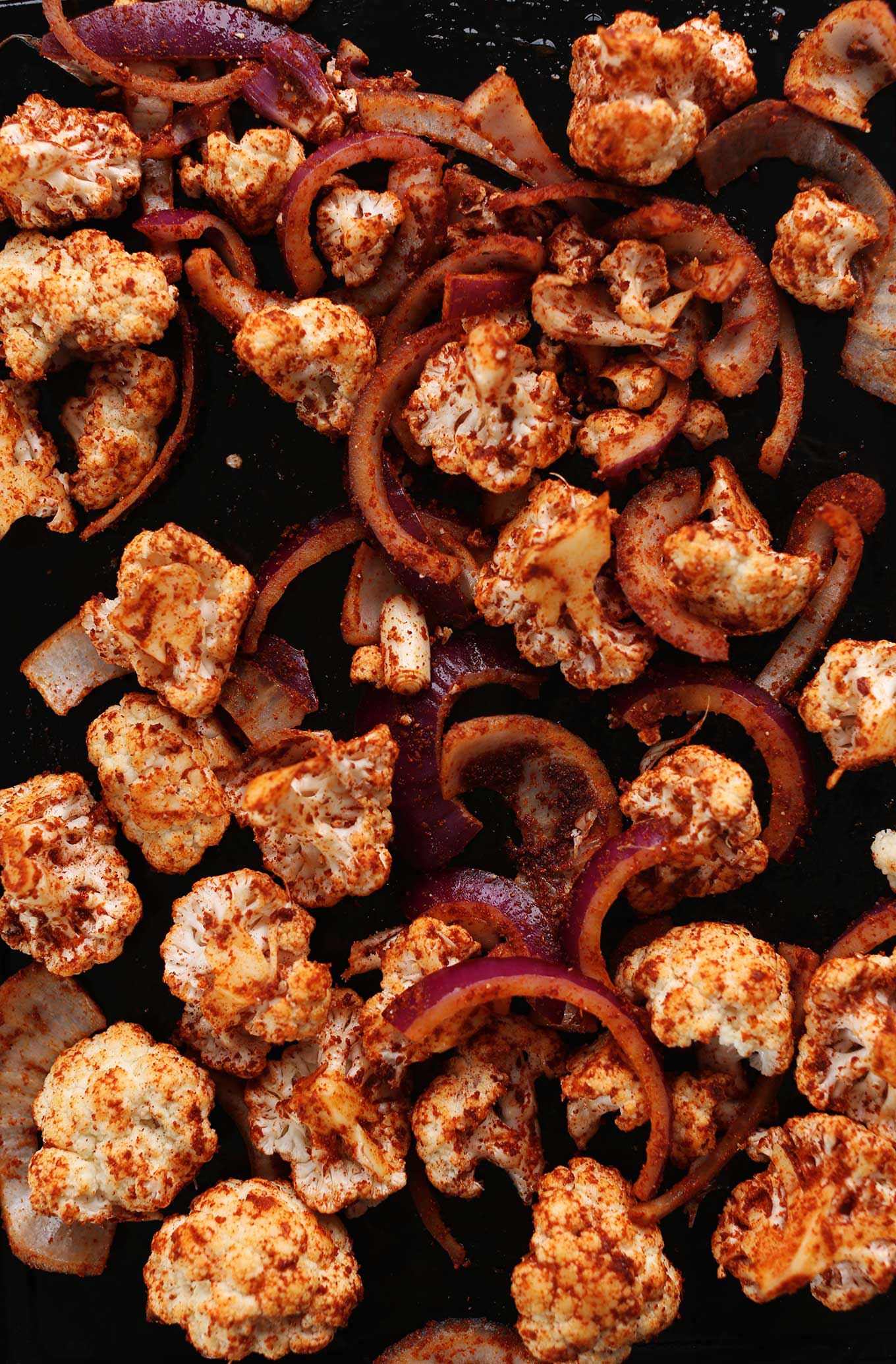 Baking sheet filled with cauliflower and red onions coated in masala spice blend