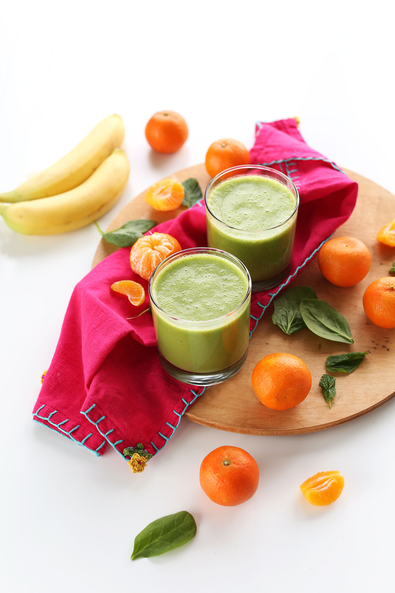 Glasses of our Coconut Clementine Smoothie on a cutting board with ingredients used to make the recipe