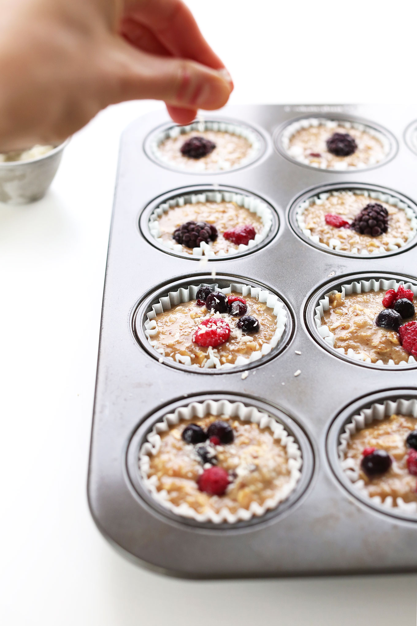 Sprinkling shredded coconut over Vegan Gluten-Free Berry Coconut Muffins