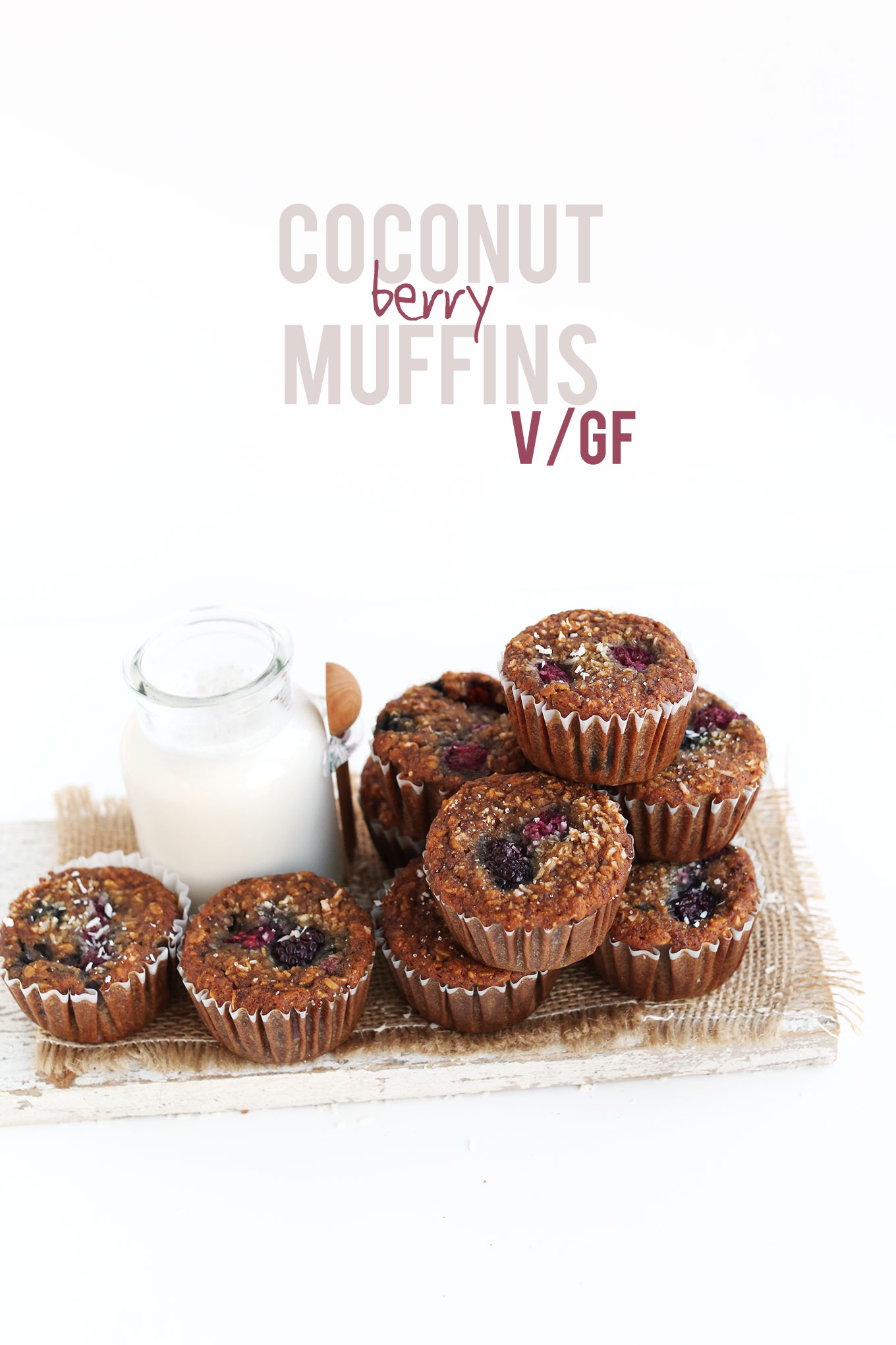 Wood cutting board with a batch of our Coconut Berry Muffins and a glass of almond milk