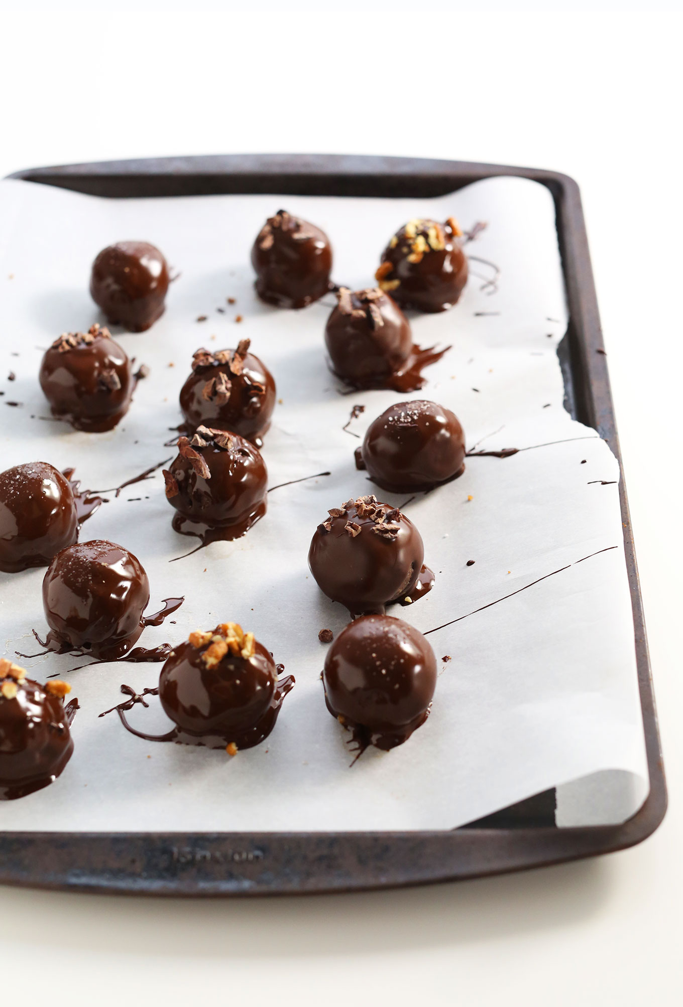 Parchment-lined baking sheet with homemade vegan truffles freshly drizzled with dark chocolate