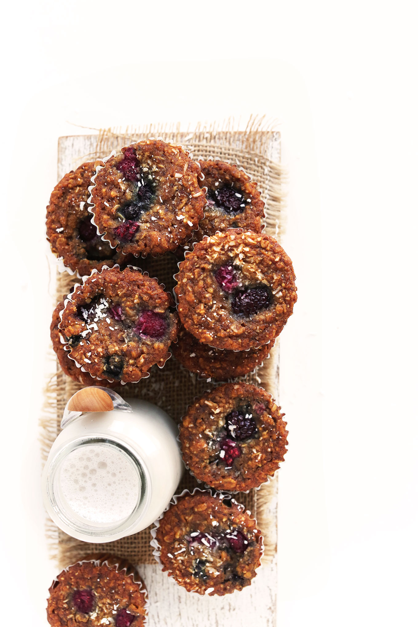 Batch of our simple Vegan Berry Coconut Muffins recipe on a wood board with nut milk