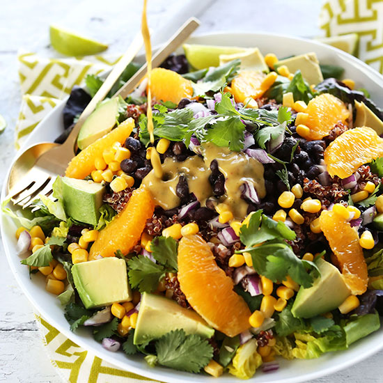 Pouring Creamy Orange Chili Dressing onto a bowl of Vegan Mexican Quinoa Salad