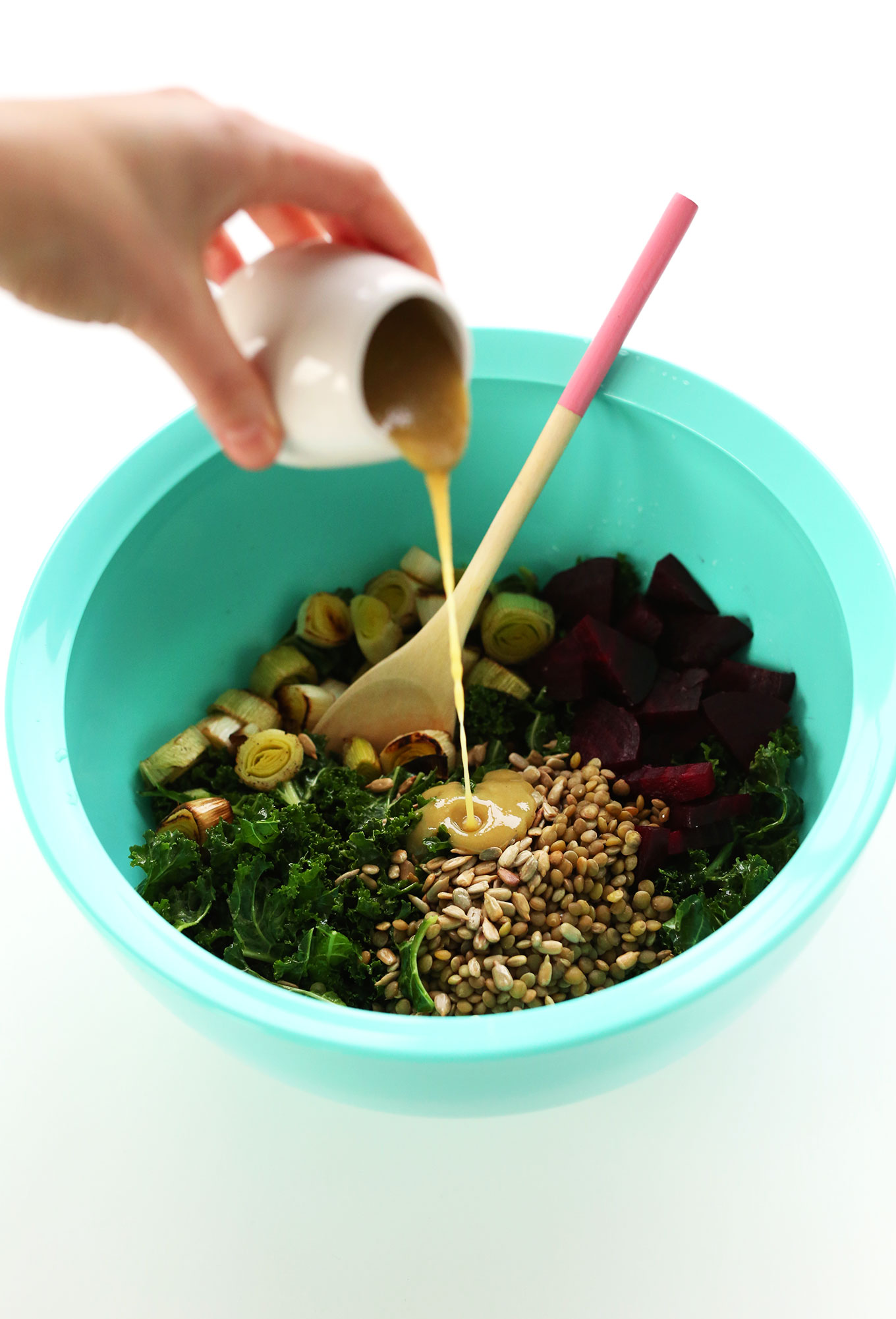 Pouring dressing onto our vegan Roasted Beet, Lentil, Kale Salad