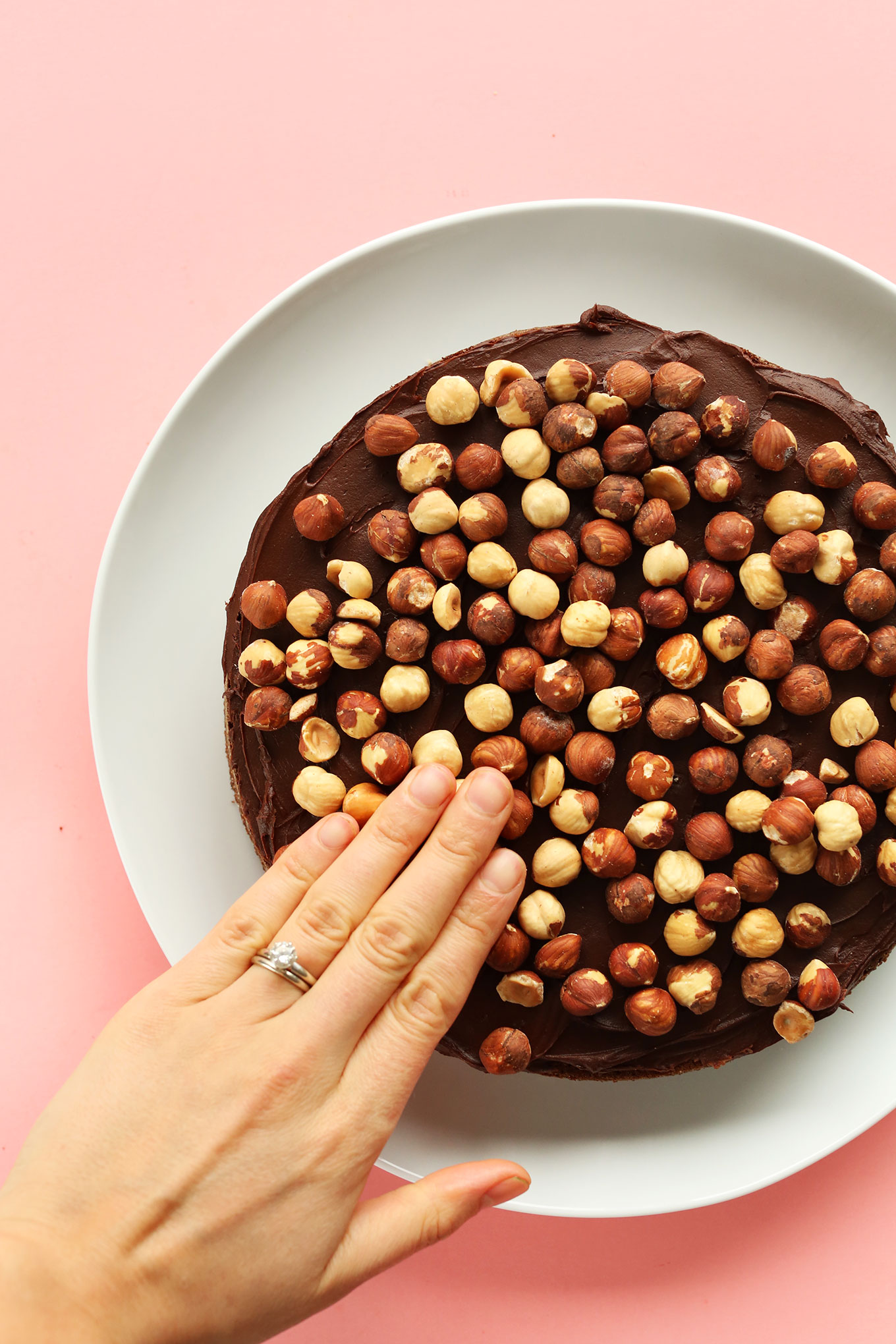 Pressing roasted hazelnuts onto our Vegan Gluten-Free Chocolate Hazelnut Cake for the middle layer