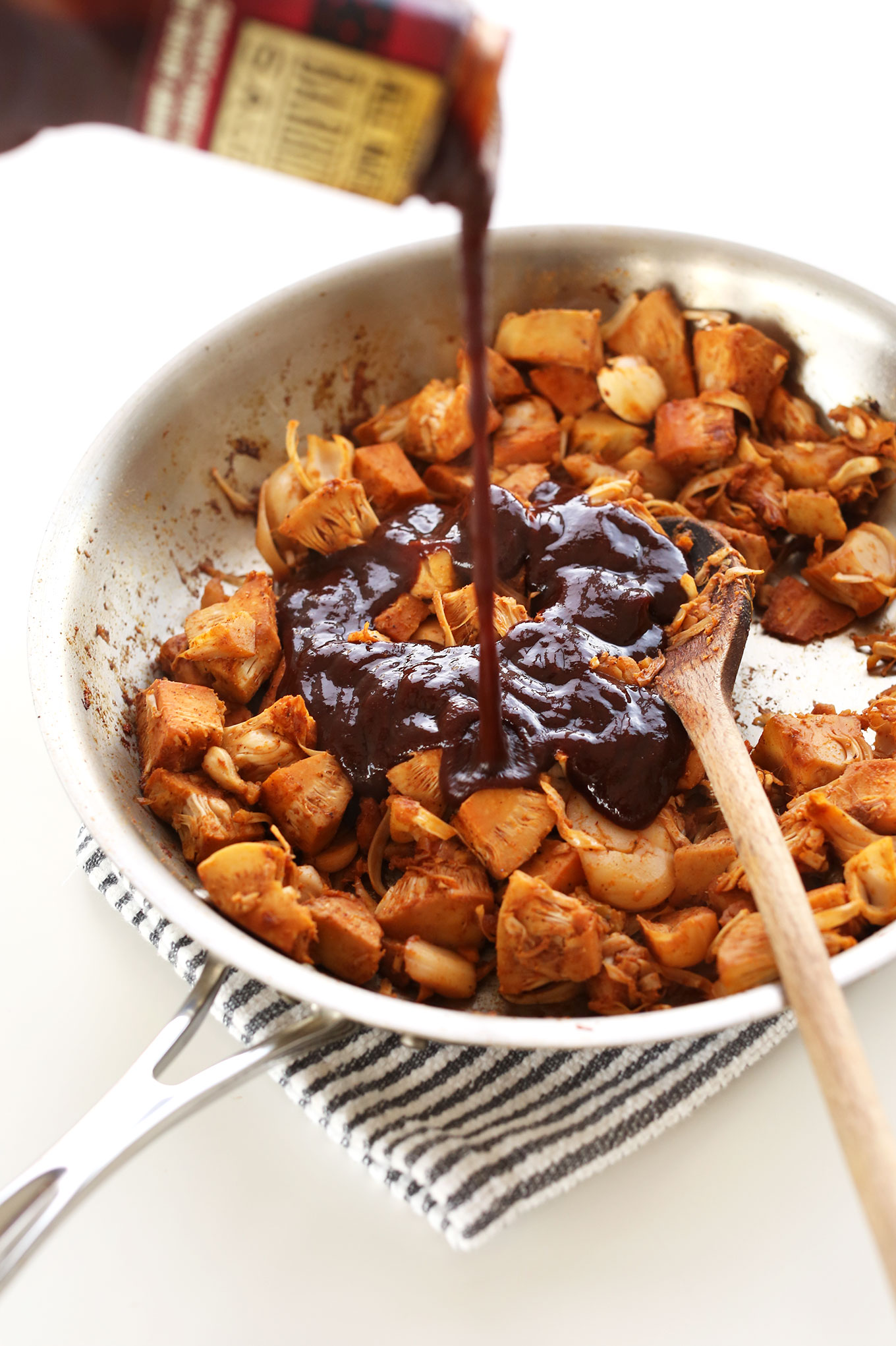 Pouring BBQ sauce into a pan of jackfruit