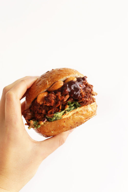 Holding up a healthy gluten-free vegan BBQ Jackfruit Sandwich