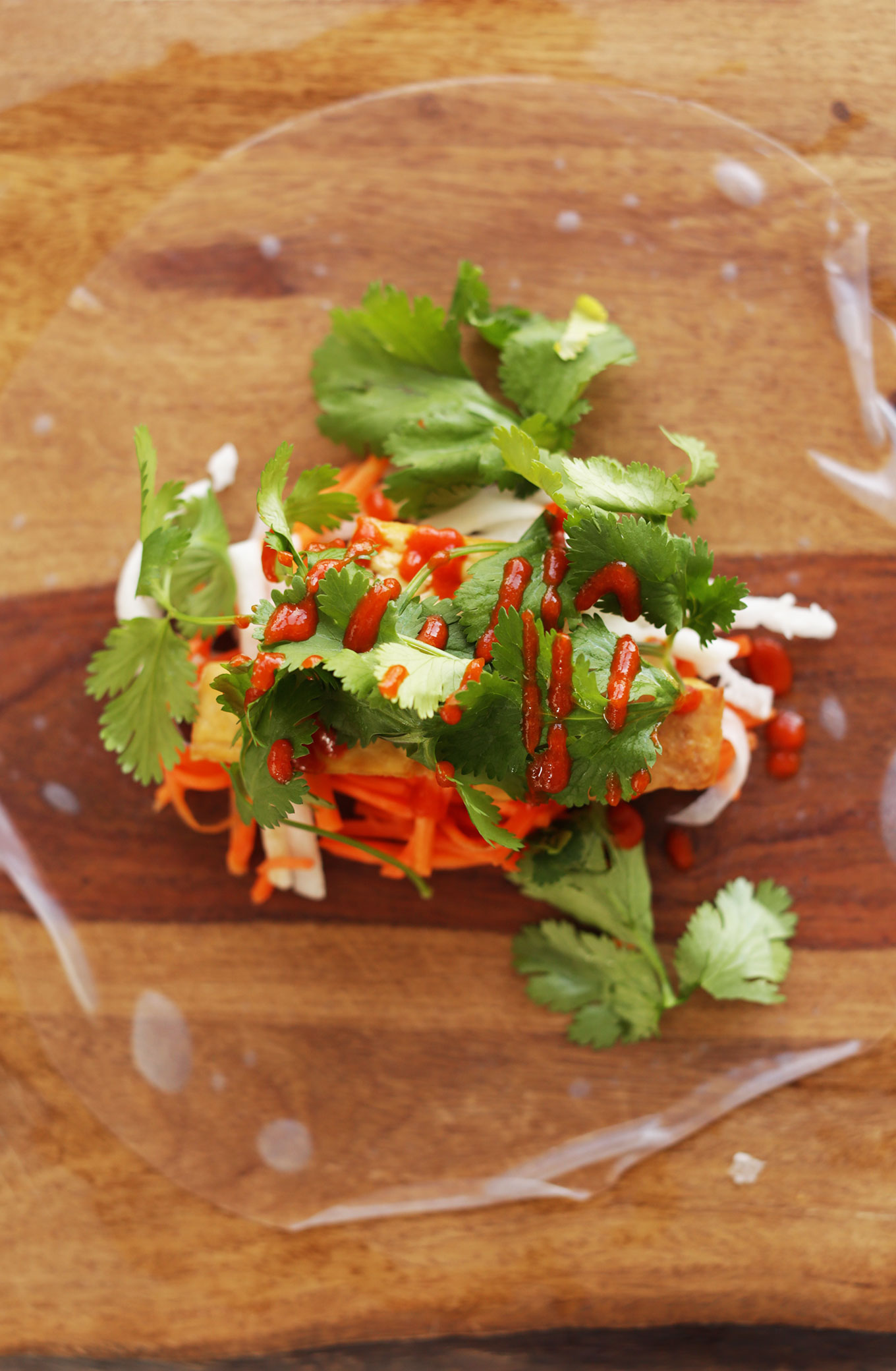 Wood cutting board with a rice paper wrapper and fillings for vegan Bahn Mi Spring Rolls