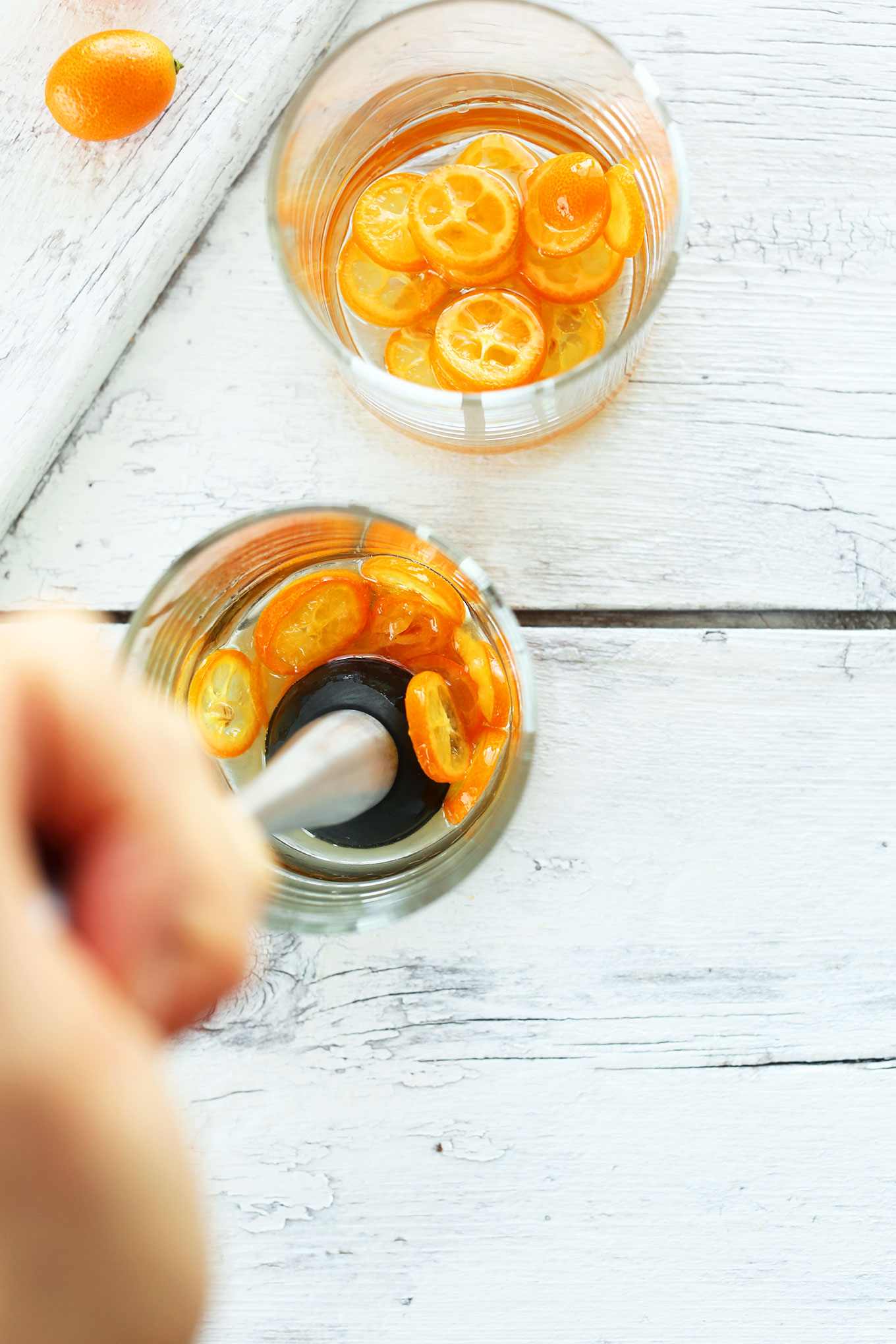 Using a muddler to mix sweetener, gin, and kumquats