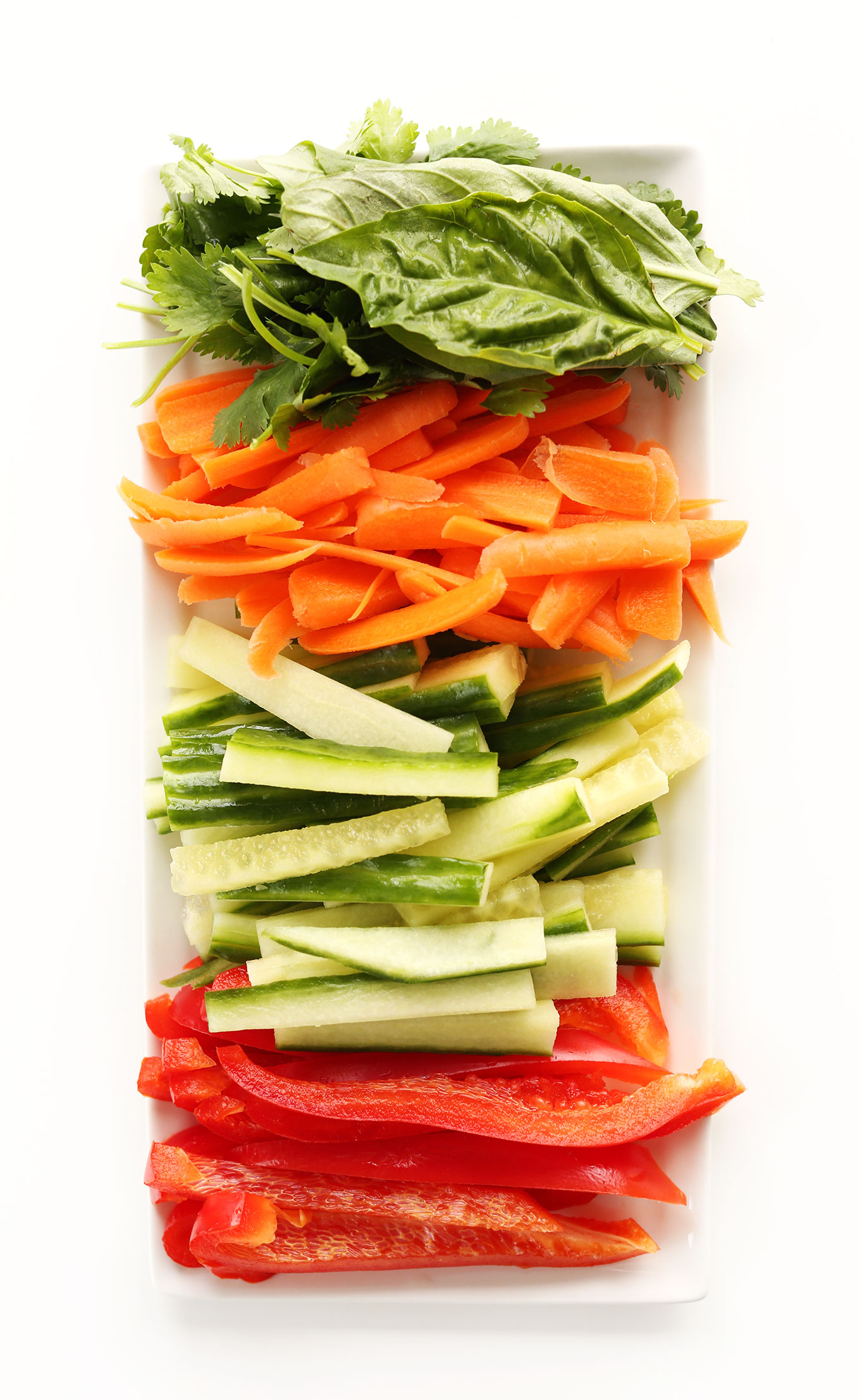 Platter of fresh basil, carrots, cucumber, and red bell pepper for making healthy Quinoa Spring Rolls
