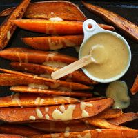 Baking sheet of Sweet Potato Wedges beside a measuring cup of No-Honey Mustard Sauce