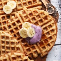 Cutting board with Coconut Yogurt Waffles topped with sliced banana and yogurt