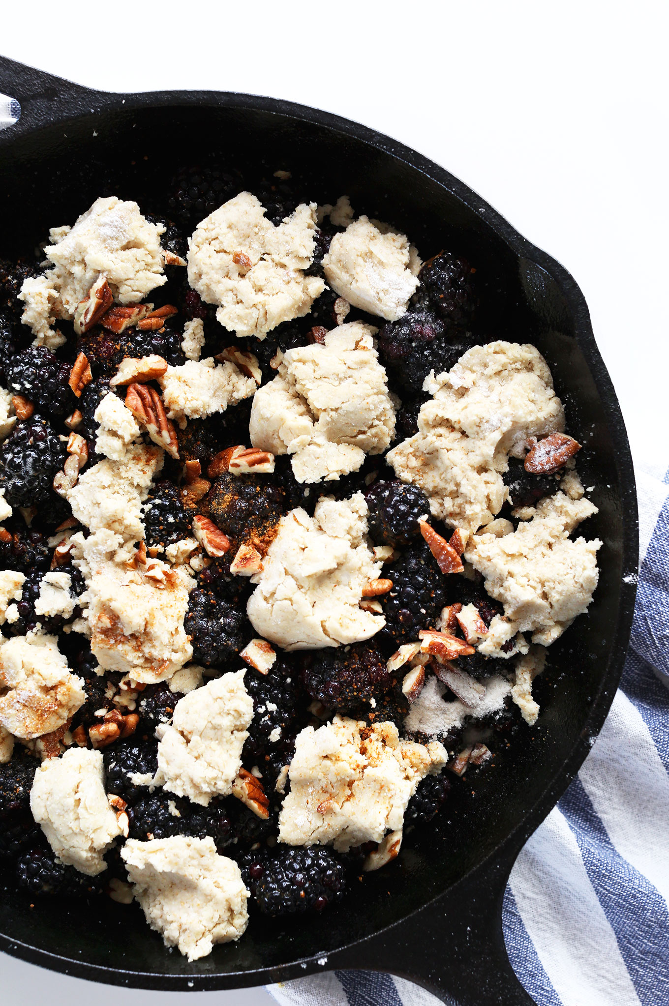 Cast-iron skillet with gluten-free biscuit layer freshly added over blackberries