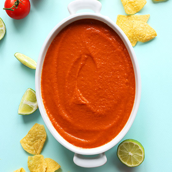 White ceramic dish filled with homemade Blended Red Salsa beside tortilla chips, limes, and tomato