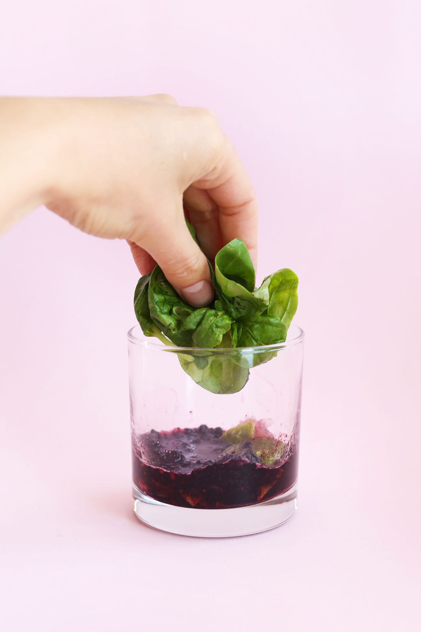 Adding basil to a cocktail glass for making Blackberry Basil Mojitos