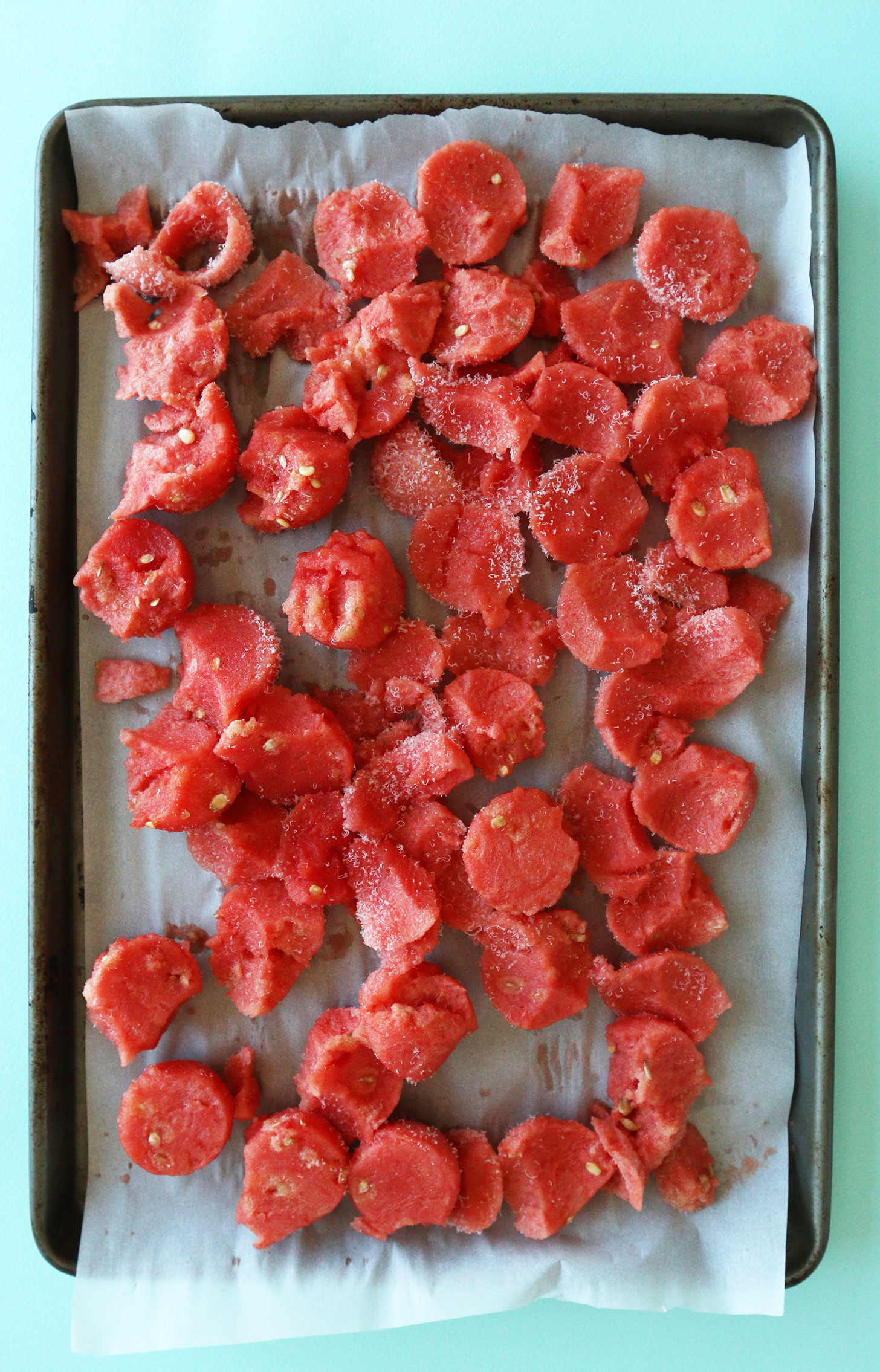 Parchment-lined baking sheet with chunks of watermelon for freezing