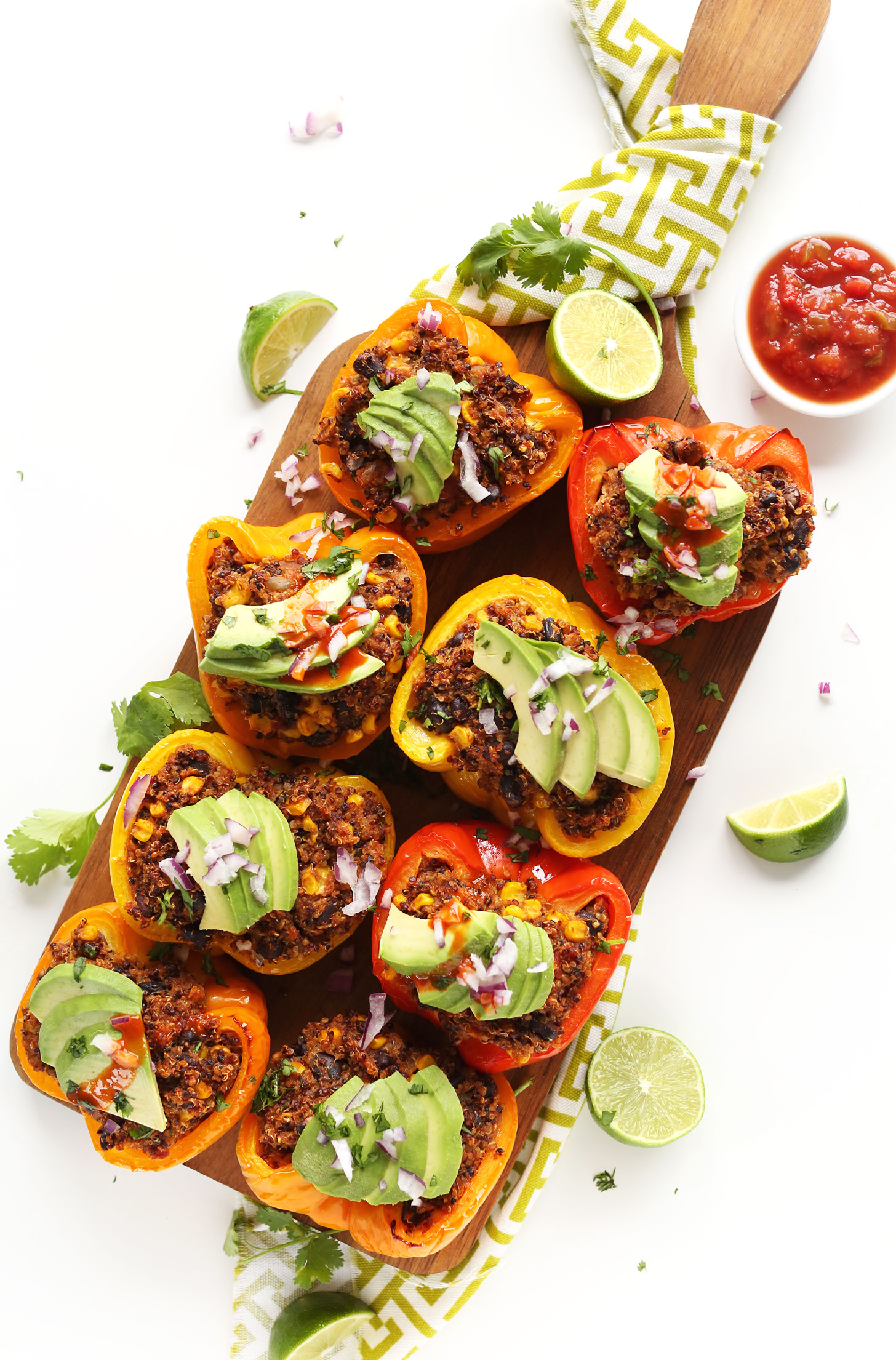 Wood platter filled with Spanish Quinoa Stuffed Peppers topped with sliced avocados