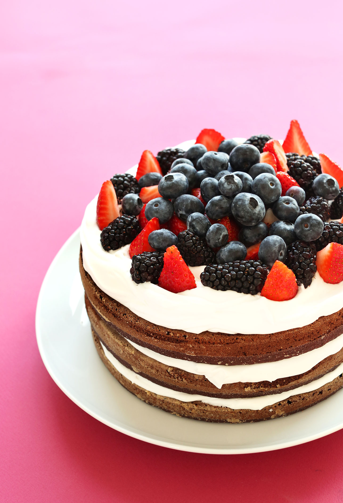 Three layer gluten-free vegan Chocolate Cake with Coconut Whipped Cream topped with fresh berries