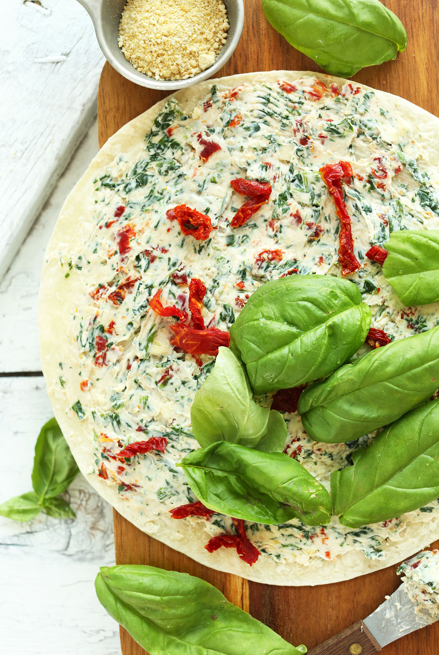 Spreading ingredients onto a tortilla for a vegan appetizer of Sun-Dried Tomato Basil Pinwheels