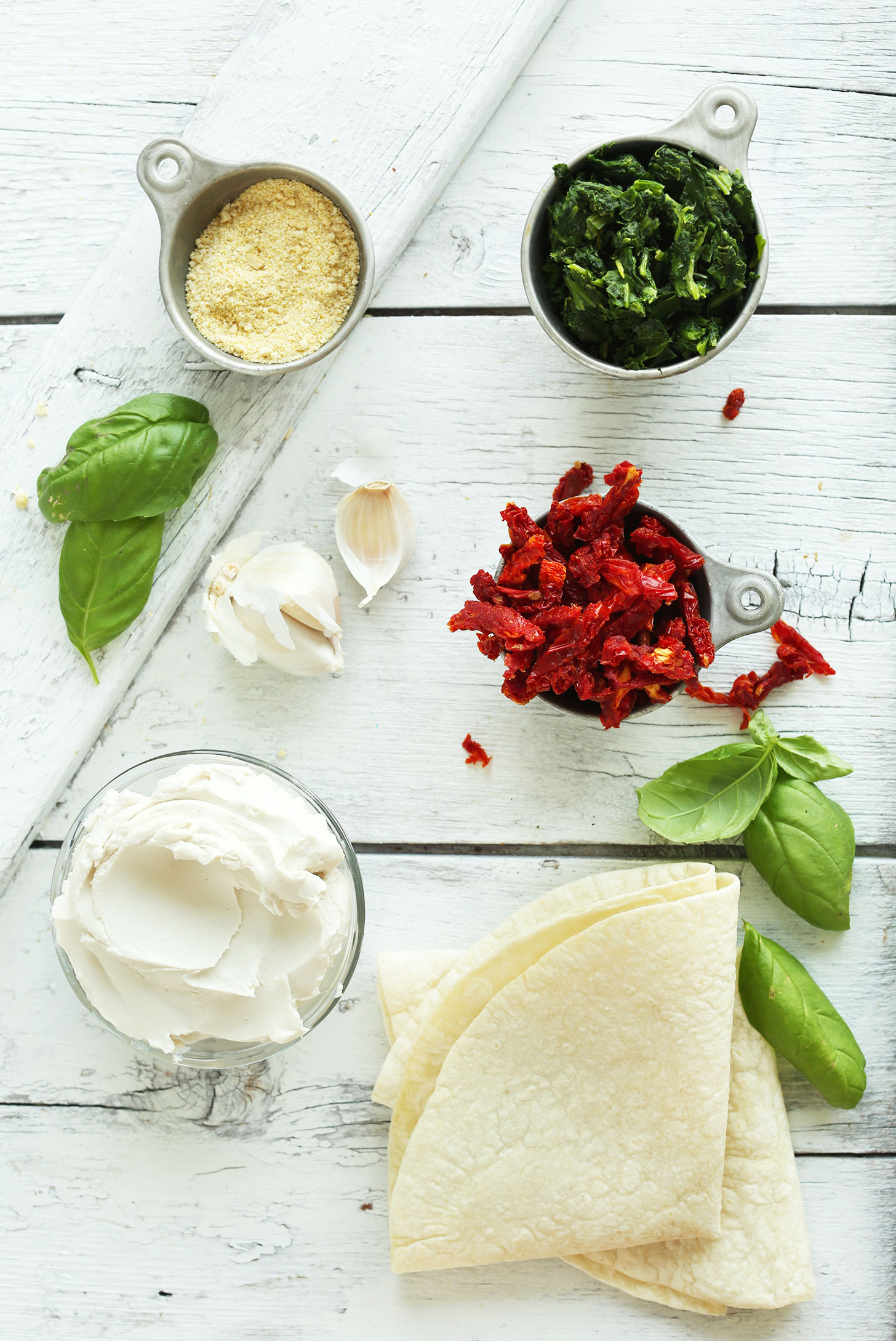 Vegan parmesan cheese, frozen spinach, sun-dried tomatoes, basil, tortillas, garlic, and vegan cream cheese for making a vegan appetizer