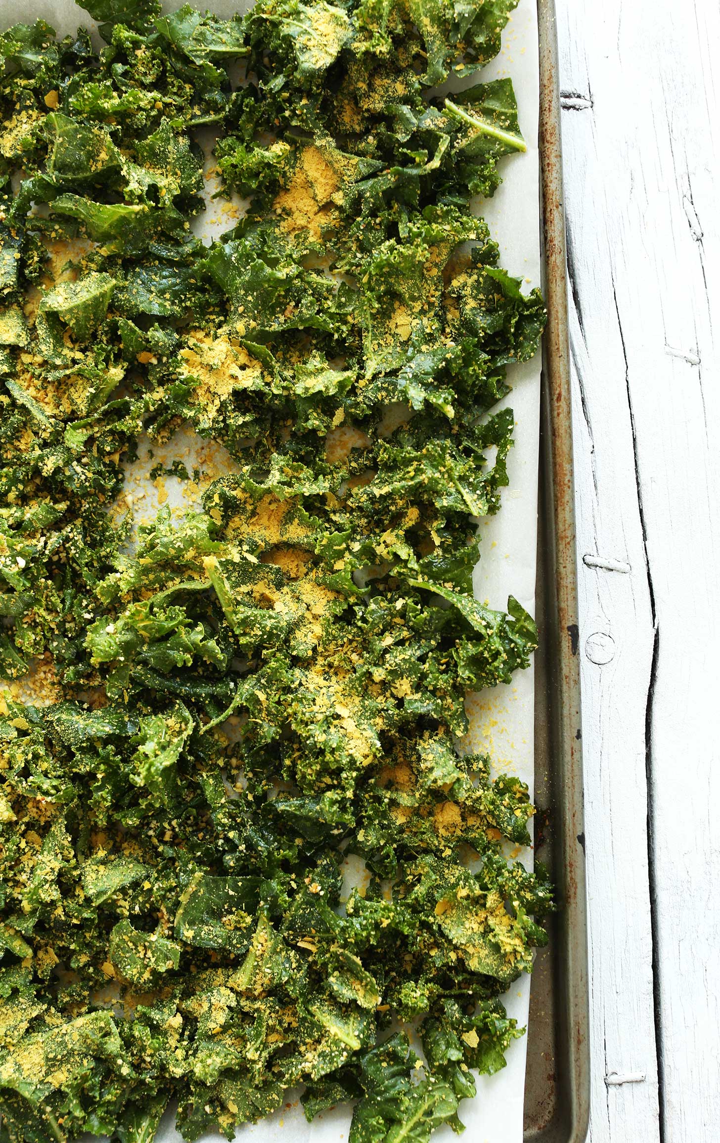 Parchment-lined baking sheet with kale, nutritional yeast, and spices for making homemade kale chips