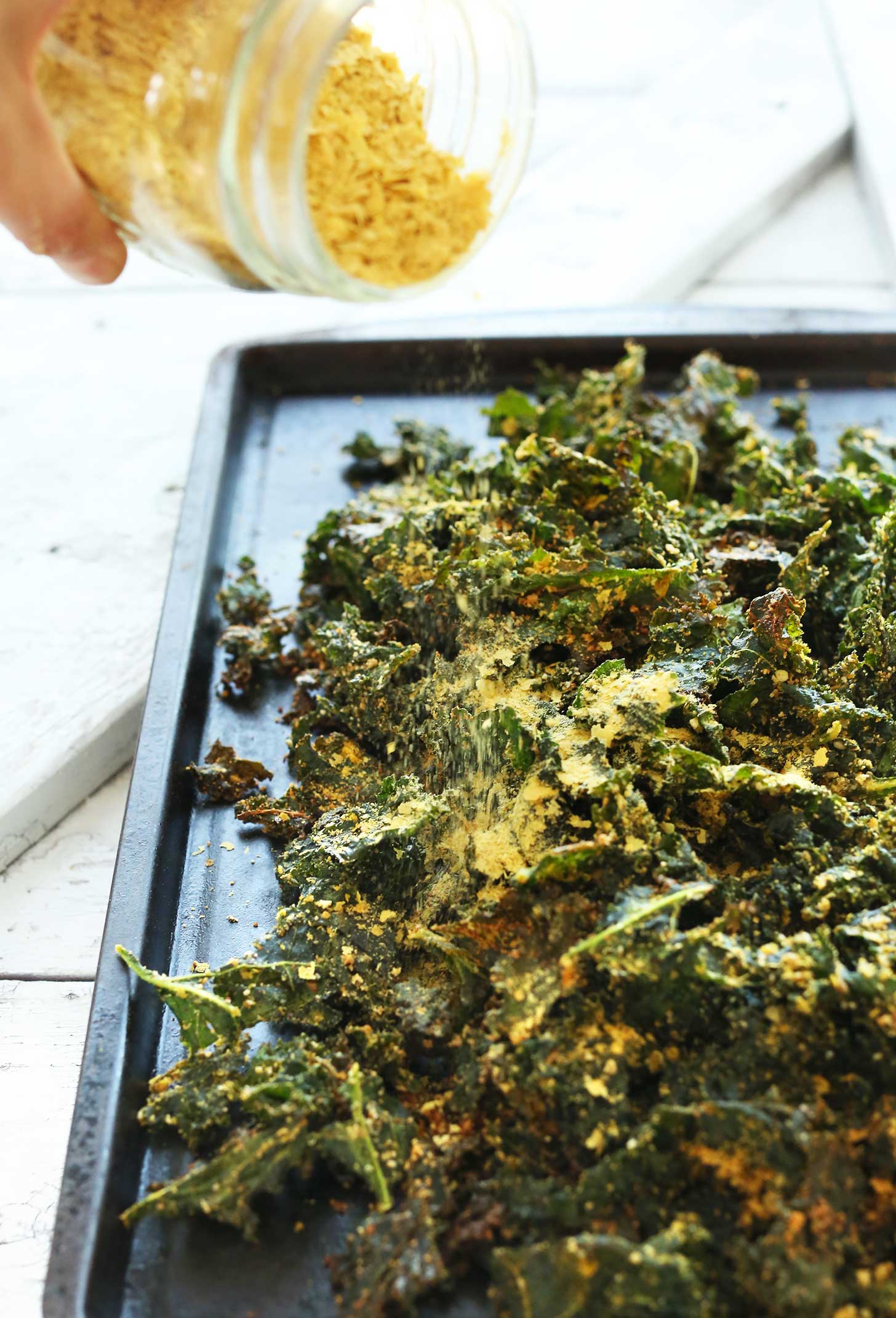 Sprinkling nutritional yeast onto kale chips for a delicious vegan snack recipe
