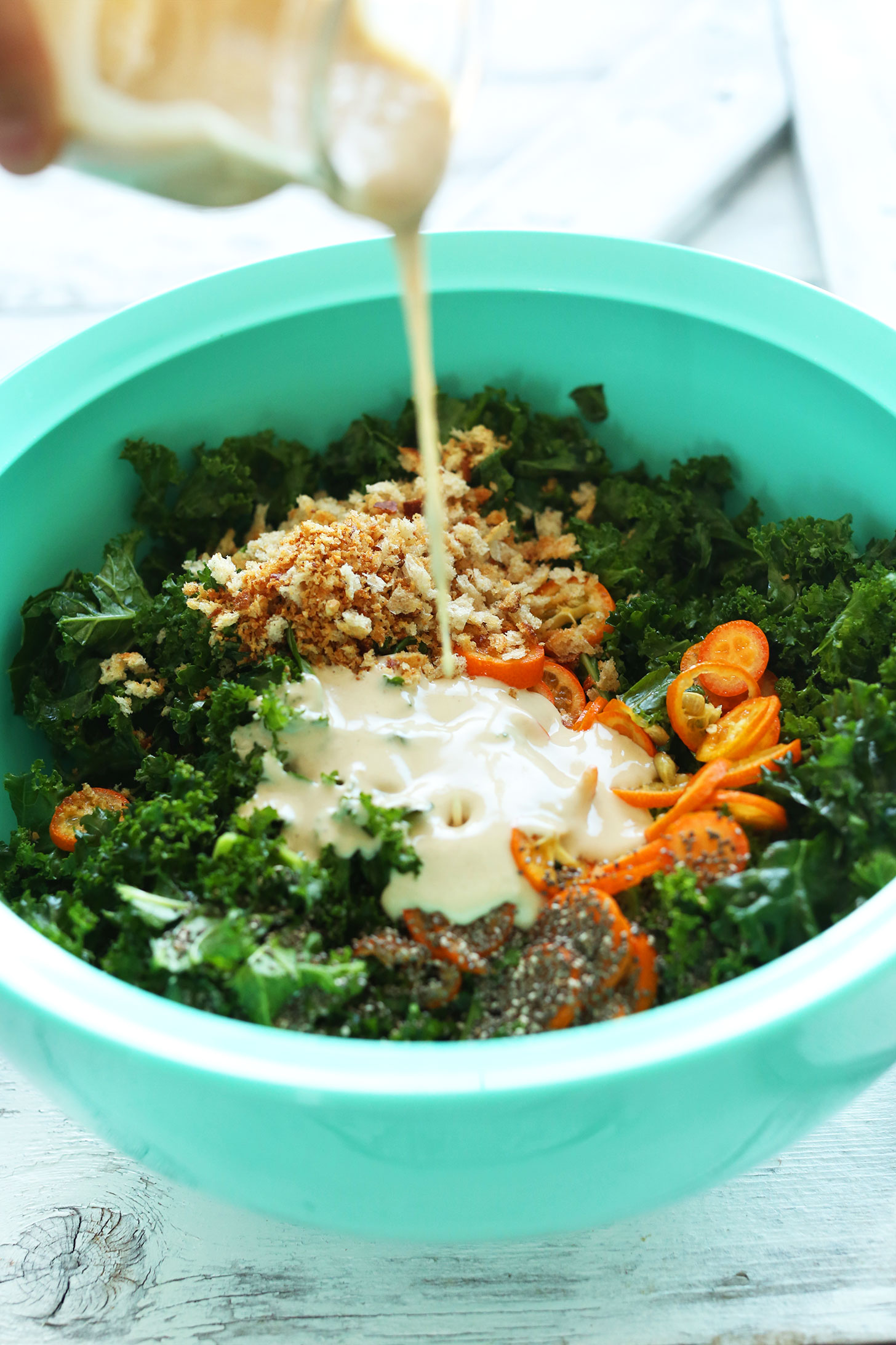 Pouring Tahini Dressing onto our delicious vegan Kale Salad with Kumquats