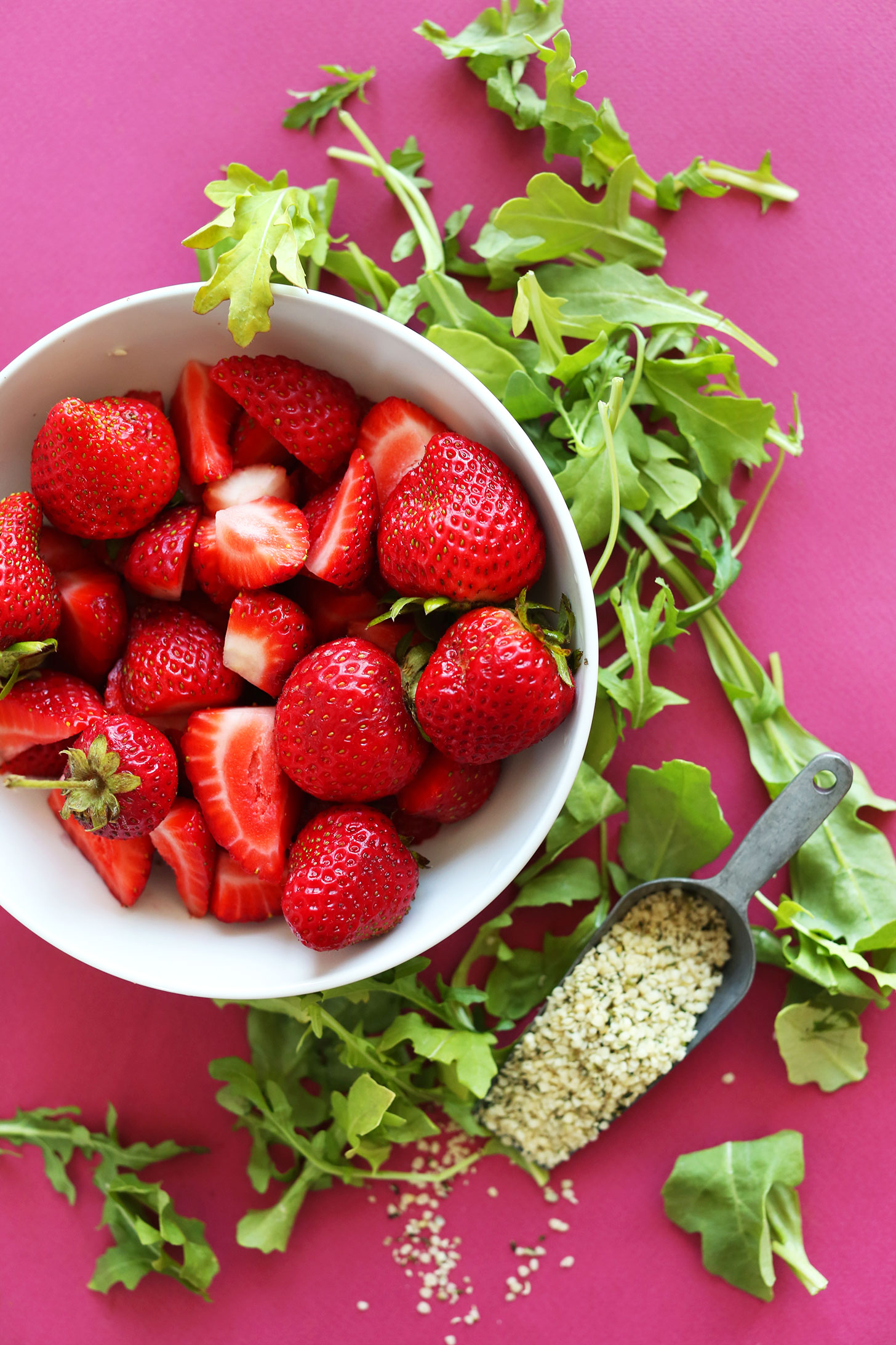 Bowl of fresh strawberries surrounded by fresh arugula and hemp seeds