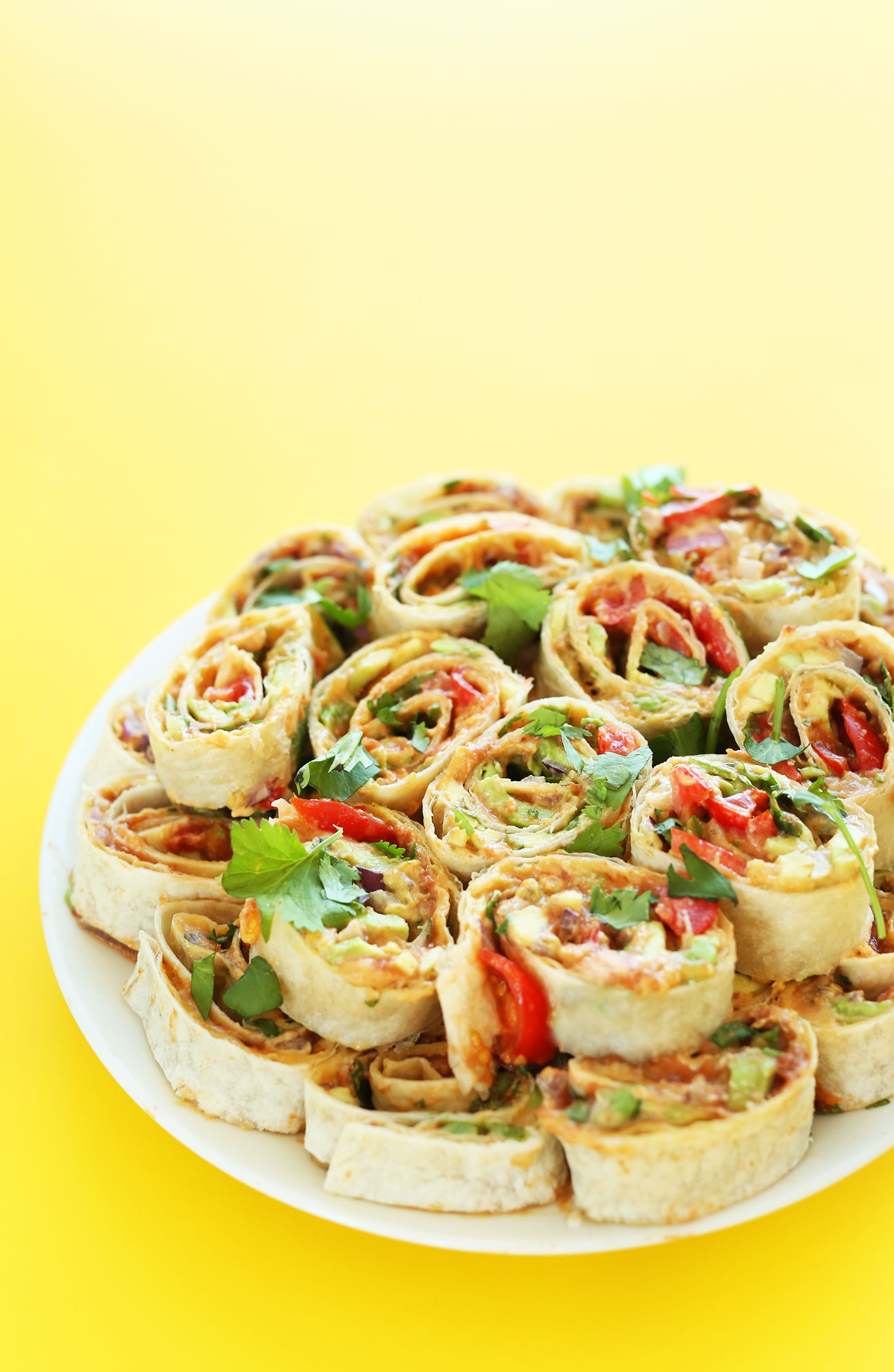 Plate filled with our Mexican Pinwheels recipe with refried beans, avocado, onion, cilantro, and tomato